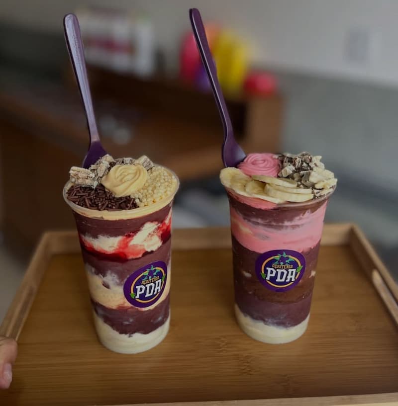 Dois copos de açaí em camadas com creme, banana, paçoca, granulado e chocolate