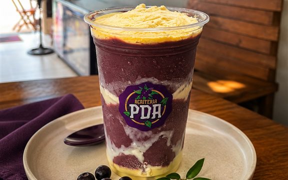 Copo da Açaíteria PDA em camadas de açaí, creme e paçoca, servido no prato
